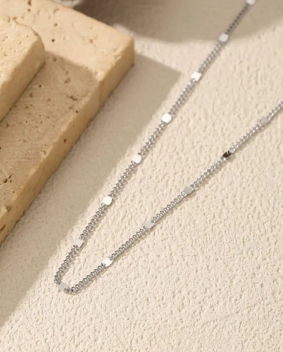 Station Chain Necklace in 925 Sterling Silver - draped across a cream surface beside a travertine slab