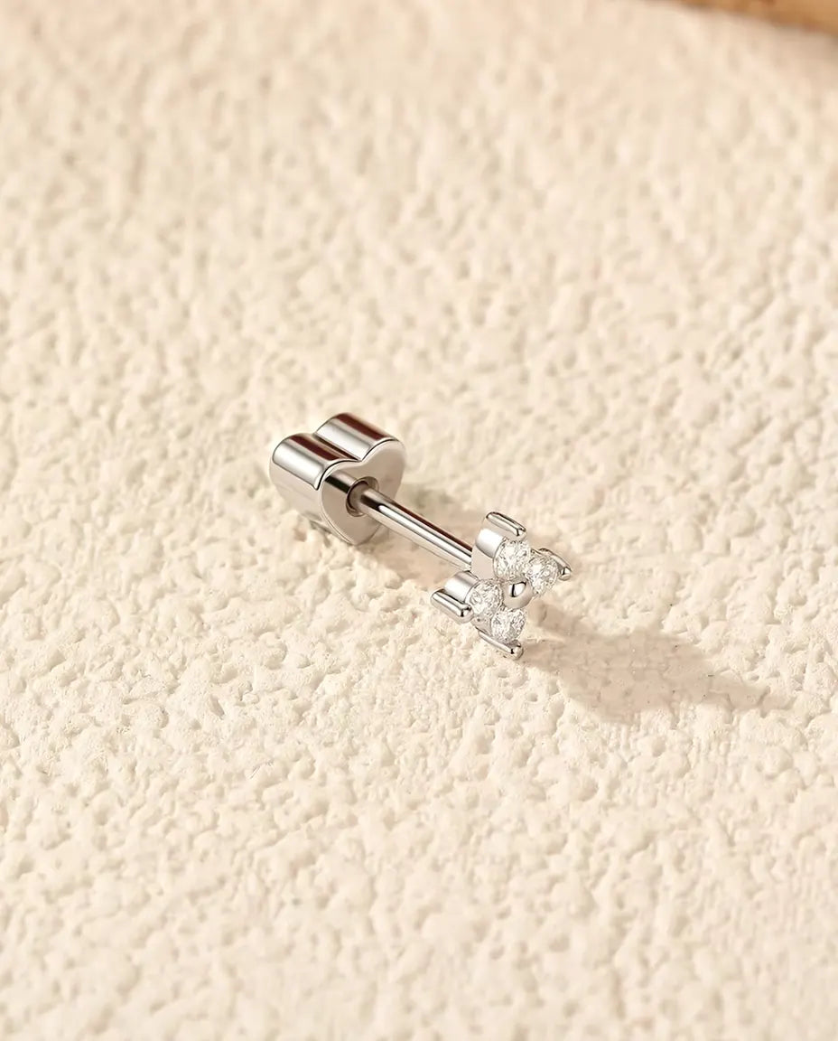 Four-Stone Moissanite Clover Stud Earrings in 925 Sterling Silver - lying on its side on a cream textured surface, heart-shaped back on the post