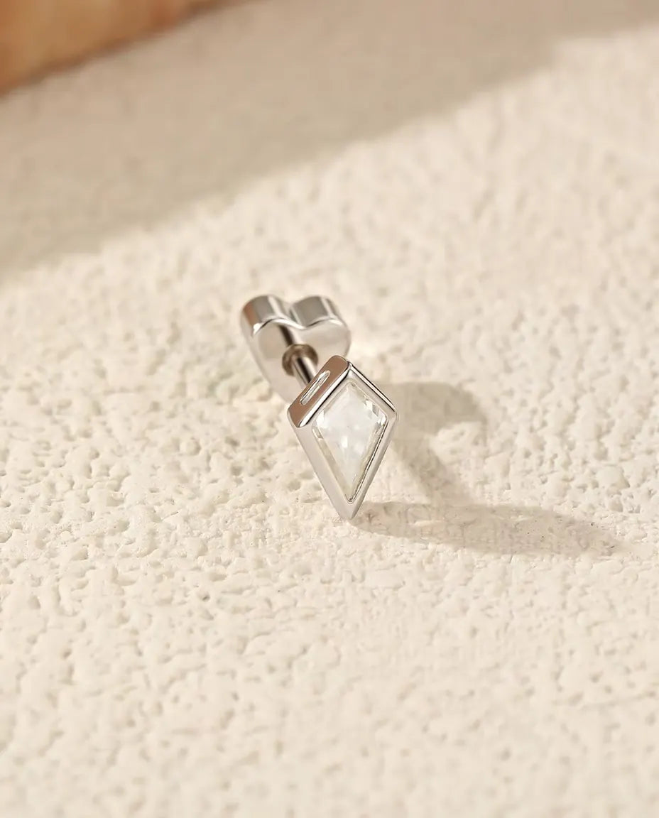Kite Cut Moissanite Stud Earrings in 925 Sterling Silver - lying on its side on a cream textured surface, heart-shaped back on the post