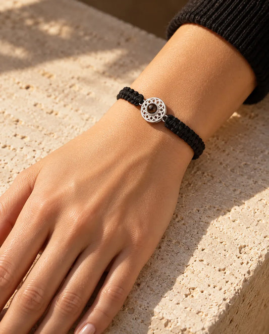 Woman wearing the black braided cord bracelet with a silver tone round charm on her wrist in warm sunlight