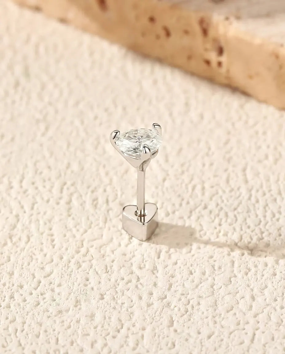 Round Moissanite Three-Prong Stud Earrings in 925 Sterling Silver - standing upright on its heart-shaped back on a cream textured surface