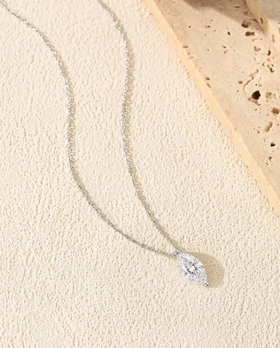 1 ct Marquise Moissanite Necklace in 925 Sterling Silver - laid in a soft curve on a cream textured surface