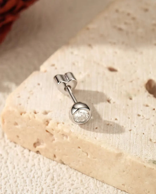 Bezel Moissanite Stud Earrings in 925 Sterling Silver - lying on a cream textured surface beside a travertine slab