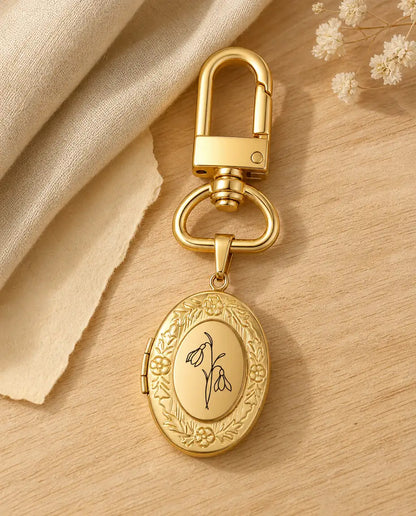 Gold birth flower photo locket keychain engraved with a snowdrop on a wood table