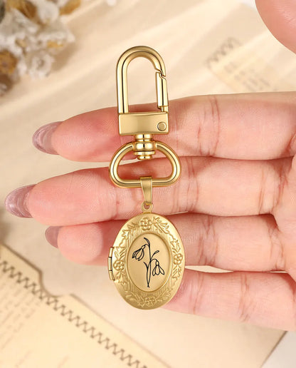 Hand holding a gold birth flower locket keychain