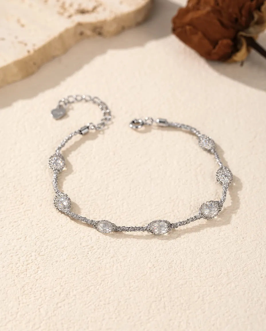 Caged Zircon Bracelet in 925 Sterling Silver - white zircon version laid flat on a cream surface