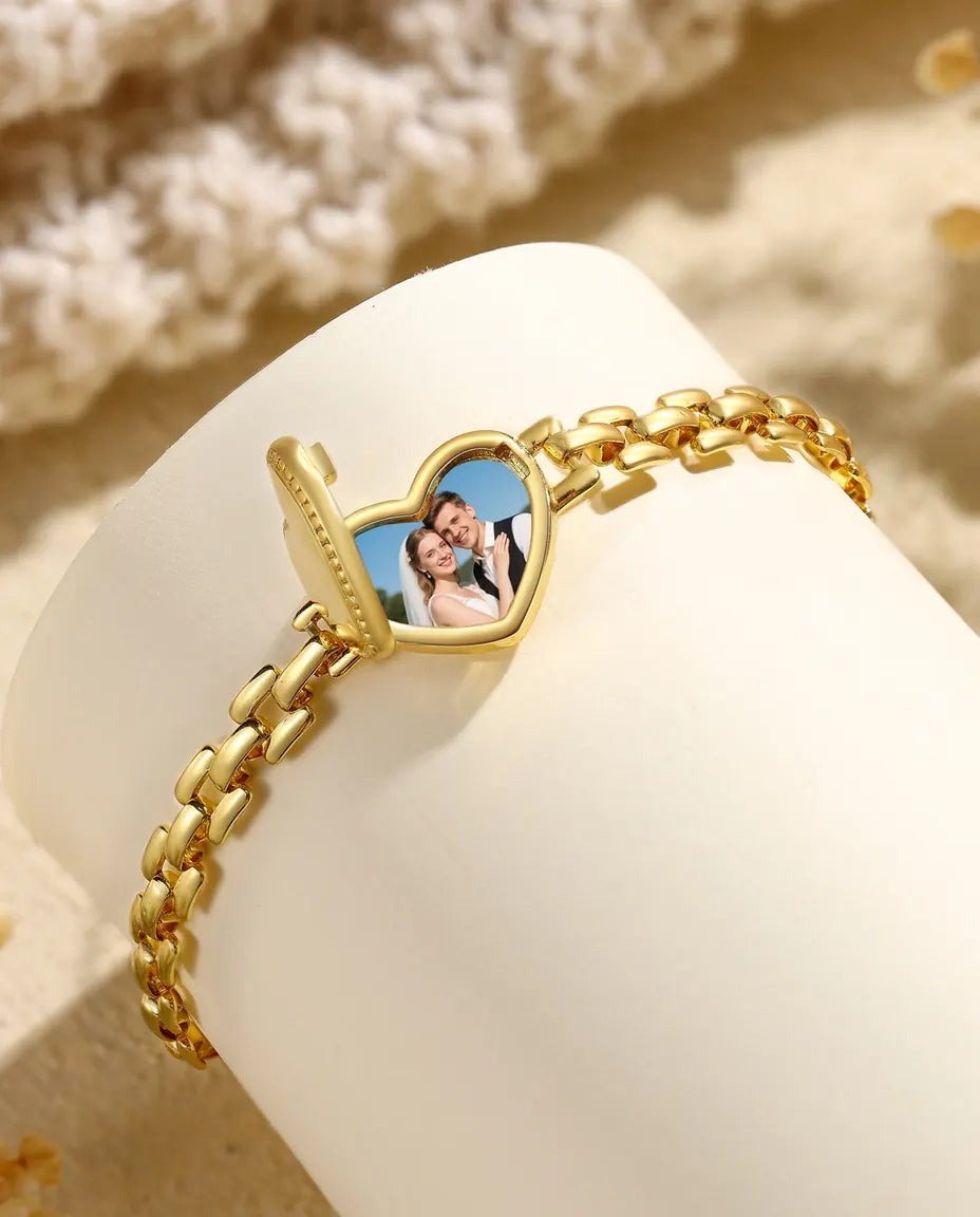 Open heart locket bracelet charm showing a photo, standing on white pedestal