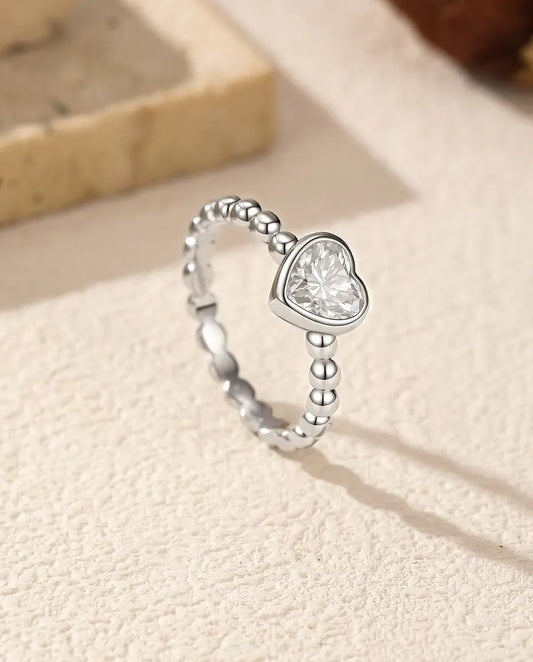 Heart Moissanite Ring in 925 Sterling Silver - standing upright on a cream textured surface