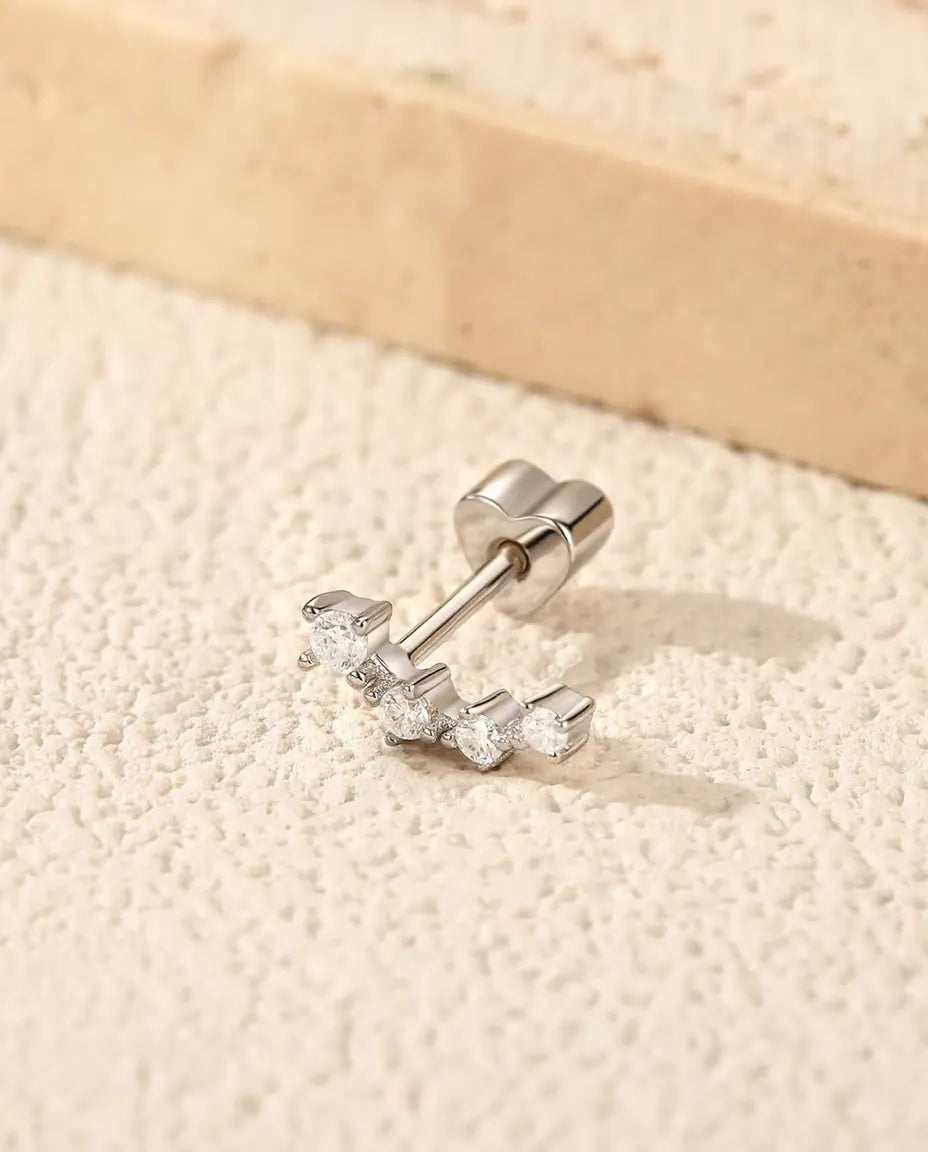 Curved Moissanite Climber Stud Earrings in 925 Sterling Silver - lying on a cream textured surface beside a travertine slab