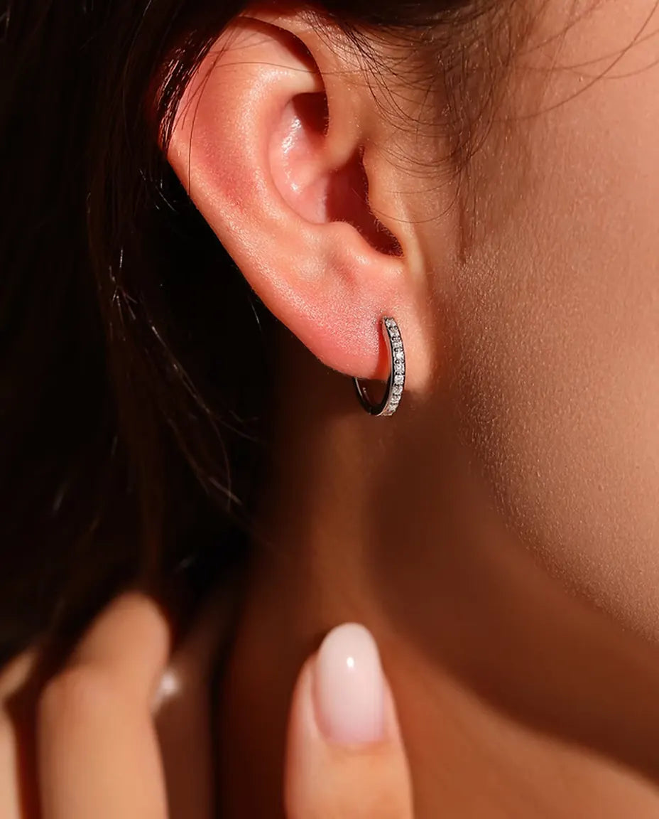 Moissanite Huggie Hoop Earrings in 925 Sterling Silver - worn on a model’s ear, hand near her face