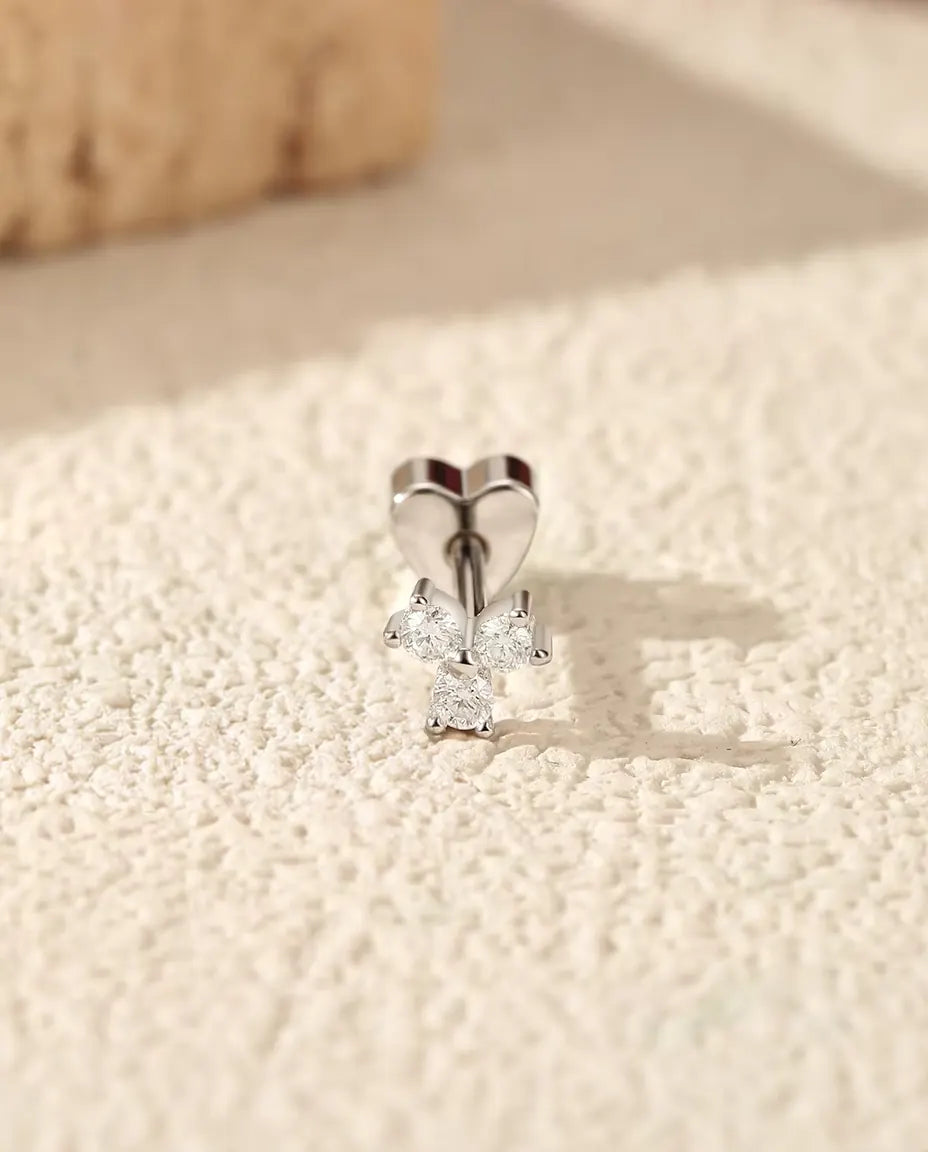 Three-Stone Moissanite Trefoil Stud Earrings in 925 Sterling Silver - standing upright on its heart-shaped back on a cream textured surface