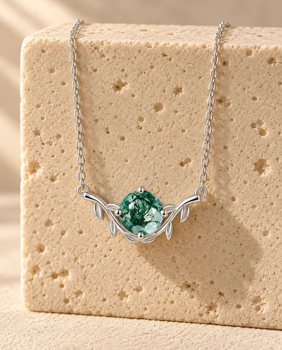 Round Cut Moss Agate Leaf Necklace - displayed on a travertine block