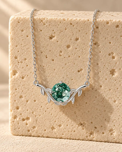 Round Cut Moss Agate Leaf Necklace - displayed on a travertine block
