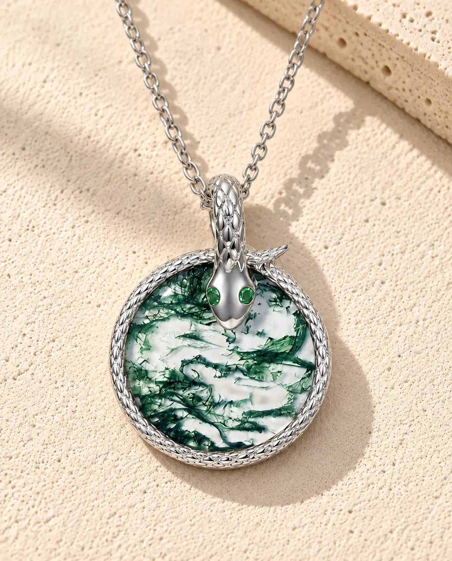Moss Agate Snake Necklace in 925 Sterling Silver - lying on a cream textured surface beside a travertine block