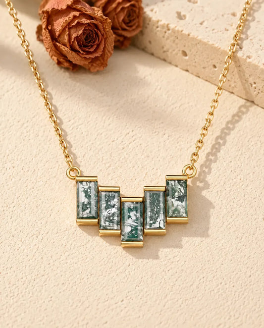 Moss Agate Baguette Necklace in 10K Gold Plated 925 Sterling Silver - lying on a cream textured surface beside a travertine block