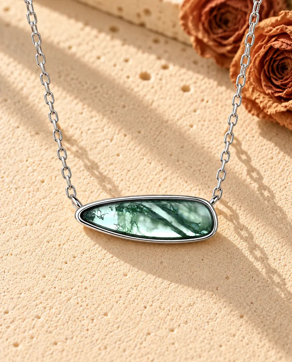 Moss Agate Bar Necklace in 925 Sterling Silver - lying on a cream textured surface beside a travertine block