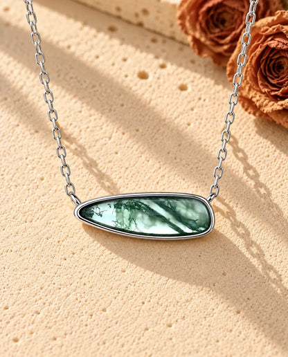 Moss Agate Bar Necklace in 925 Sterling Silver - lying on a cream textured surface beside a travertine block