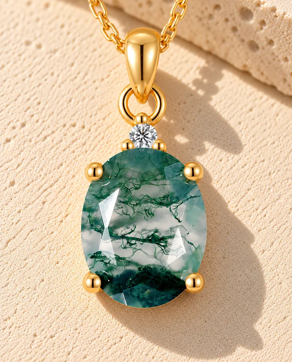 Oval Moss Agate Solitaire Necklace in Gold Plated 925 Sterling Silver - lying on a cream textured surface beside a travertine block