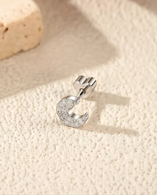 Pavé Moissanite Crescent Stud Earrings in 925 Sterling Silver - lying on its side on a cream textured surface, heart-shaped back on the post