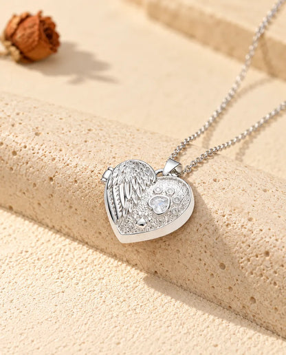 Personalized angel wing paw print heart photo locket necklace in silver tone with a heart-shaped stone paw print, resting on a travertine block