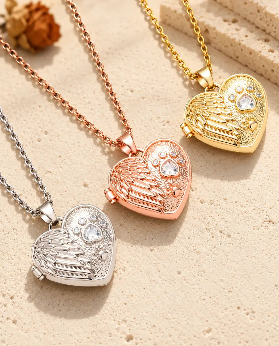 Angel wing paw print heart photo lockets in silver tone, rose gold tone and gold tone laid diagonally on cream plaster