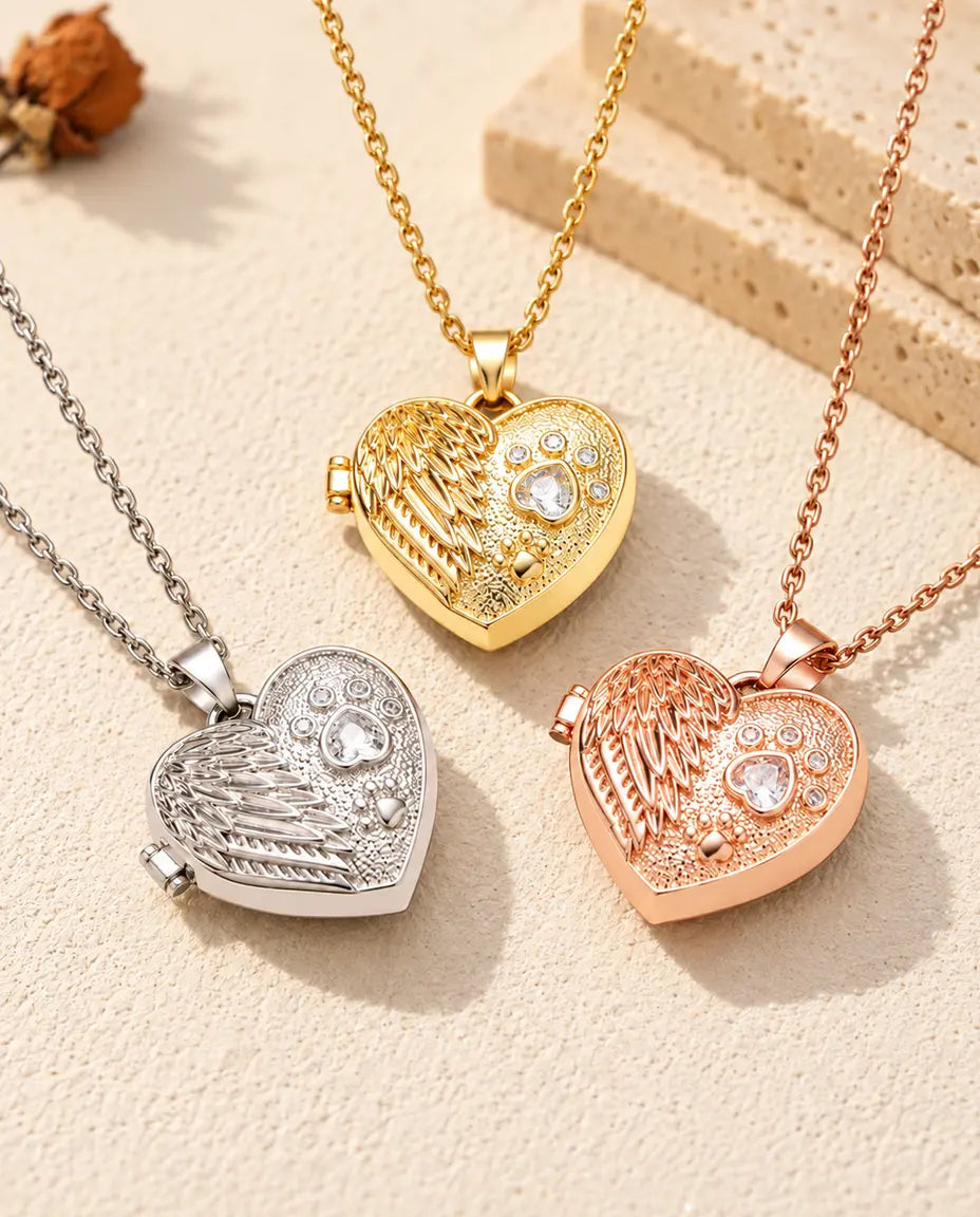 Three colors of the angel wing paw print heart photo locket necklace arranged on plaster