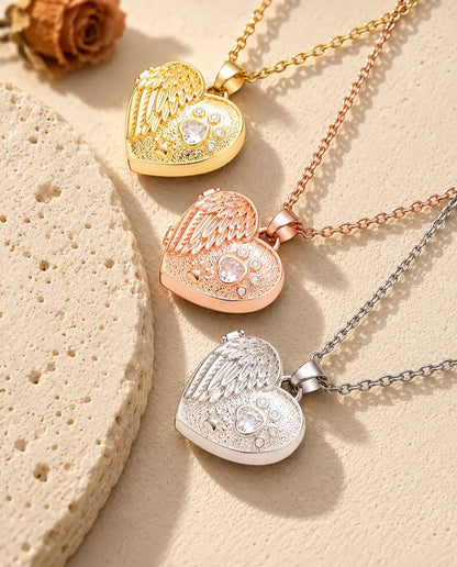 Gold tone, rose gold tone and silver tone angel wing paw print heart photo lockets stacked beside a travertine slab