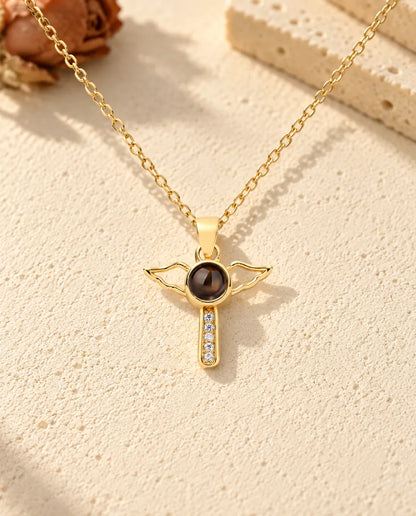 Front view of the gold tone cross with open angel wings and the projection stone at its center