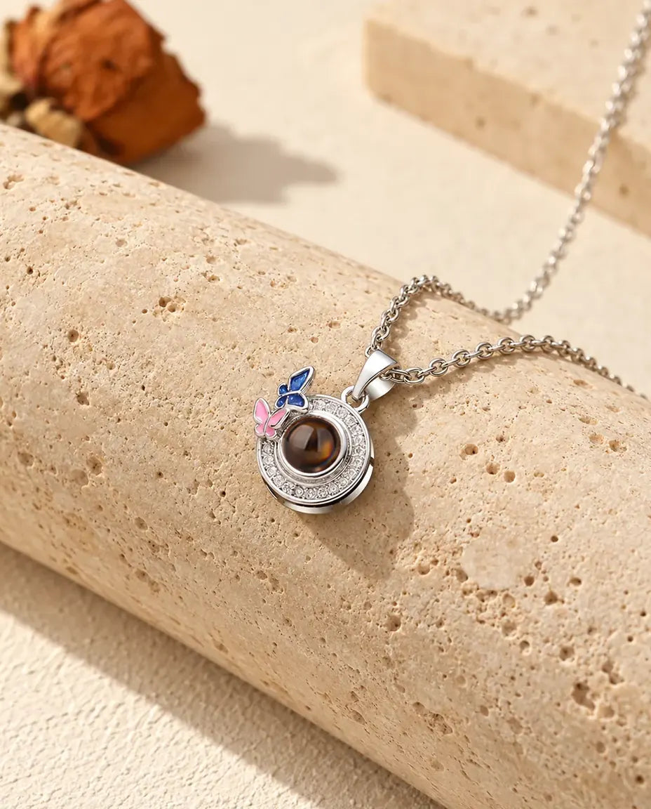 Personalized butterfly circle photo projection necklace in silver tone with navy and pink enamel butterflies, on travertine