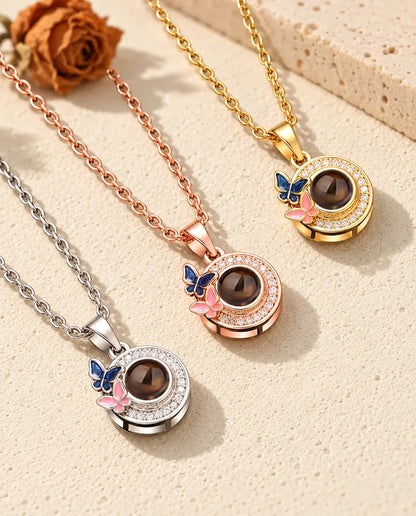 Three colors of the butterfly photo projection necklace on a diagonal on cream plaster