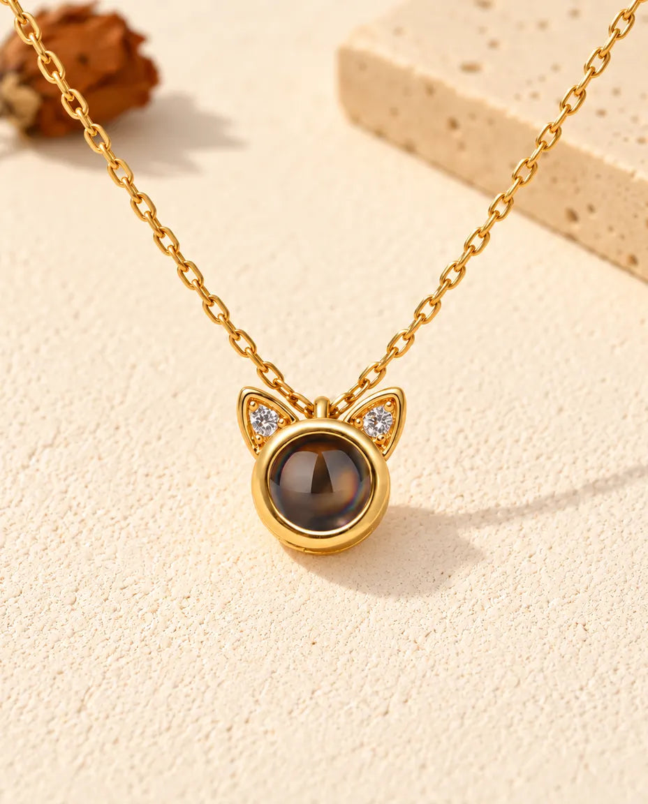 Front view of the tiny gold tone round pendant with two cat ears
