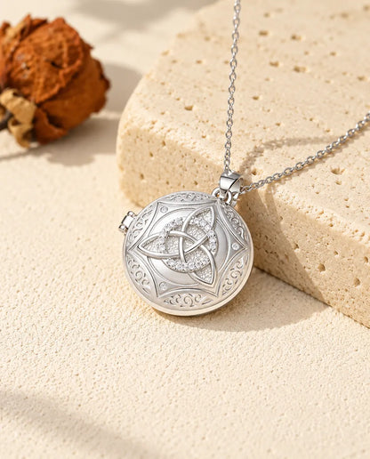 Personalized round Celtic knot photo locket necklace in silver with cubic zirconia, resting on a travertine block