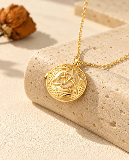 Gold tone round Celtic knot locket necklace draped over a travertine block