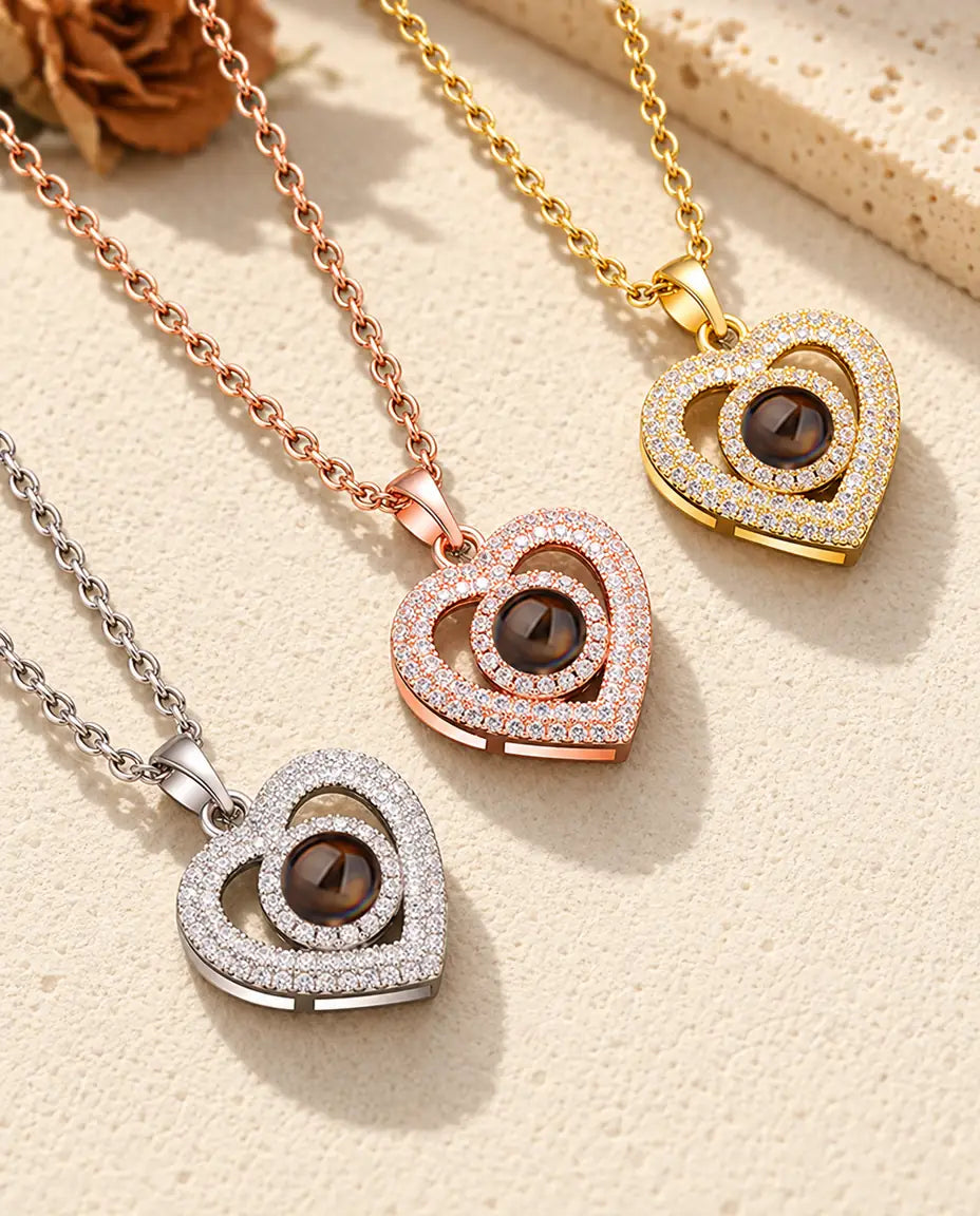Three colors of the double heart photo projection necklace on a diagonal on cream plaster