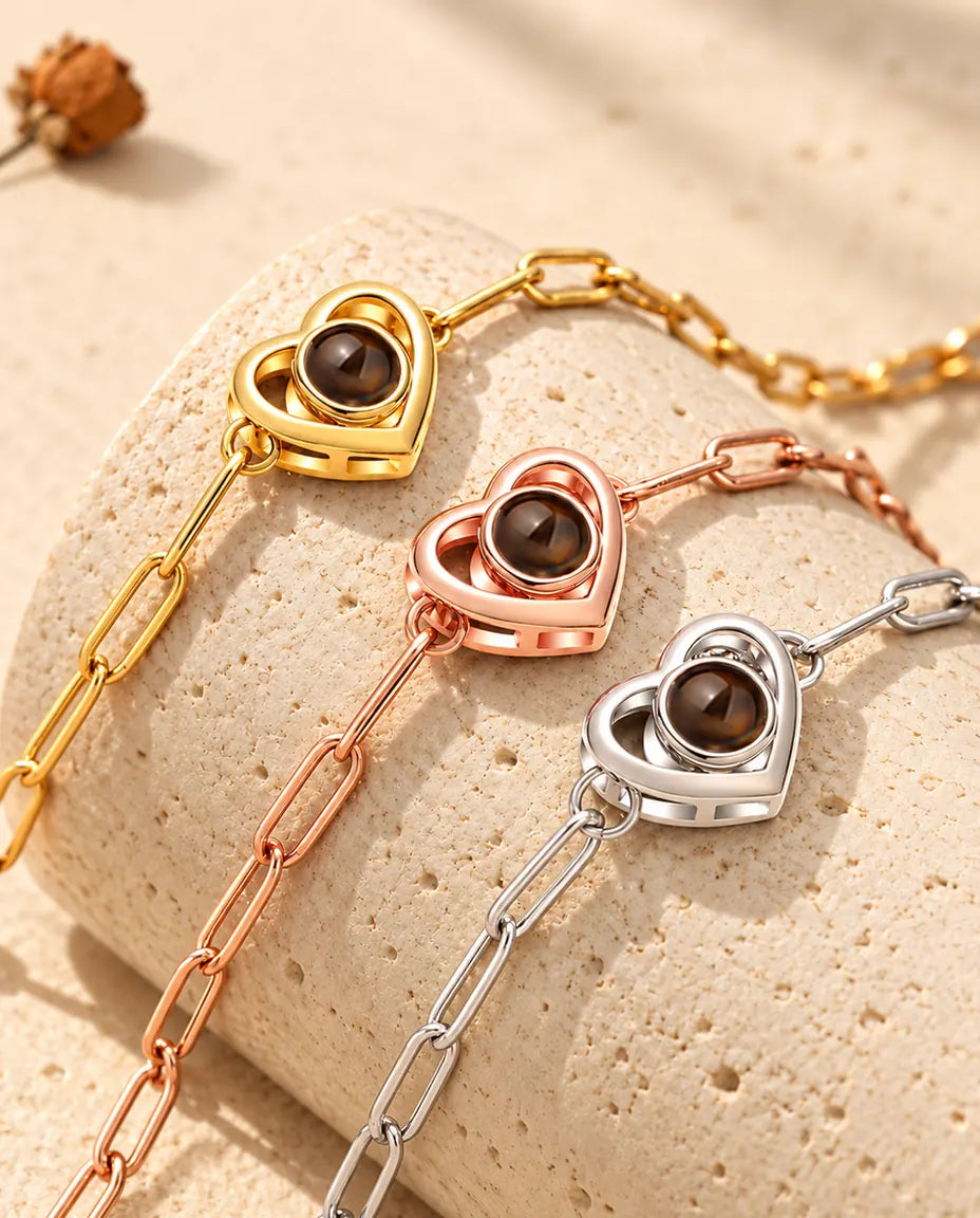 Gold tone, rose gold tone and silver tone double heart projection bracelets draped over a travertine block