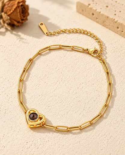 Gold tone double heart photo projection bracelet resting on cream plaster