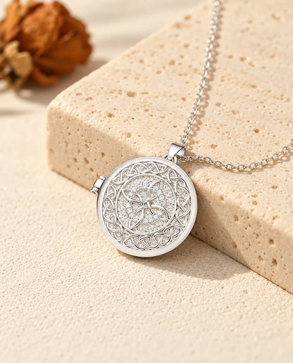 Personalized four-loop Celtic knot photo locket necklace in silver tone with a ring of cubic zirconia, resting on a travertine block