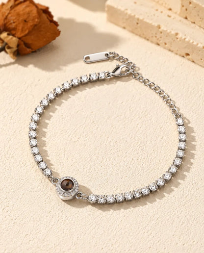 Personalized photo projection tennis bracelet in silver tone with a halo charm, lying on cream plaster