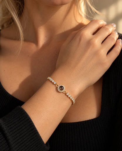 Close-up of the gold tone tennis bracelet with a halo projection charm on a wrist at the collarbone