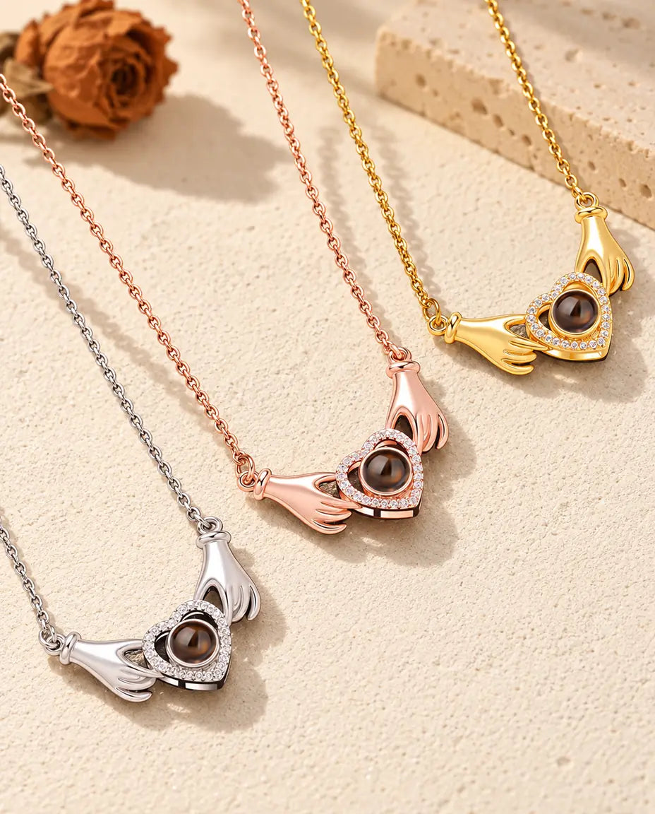 Hands holding heart projection necklaces in silver, rose gold tone and gold tone laid side by side