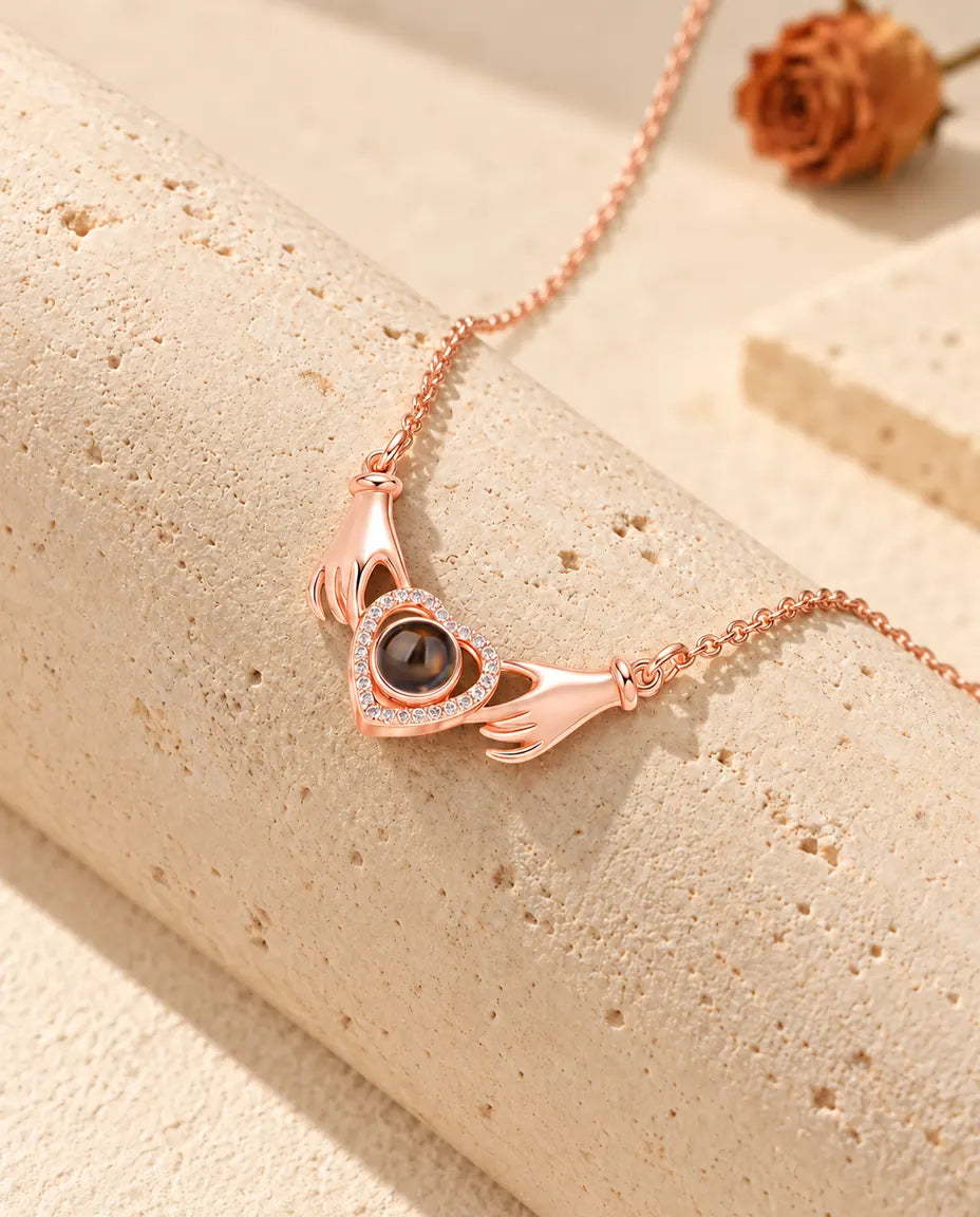 Rose gold tone hands holding heart projection necklace draped over a travertine block