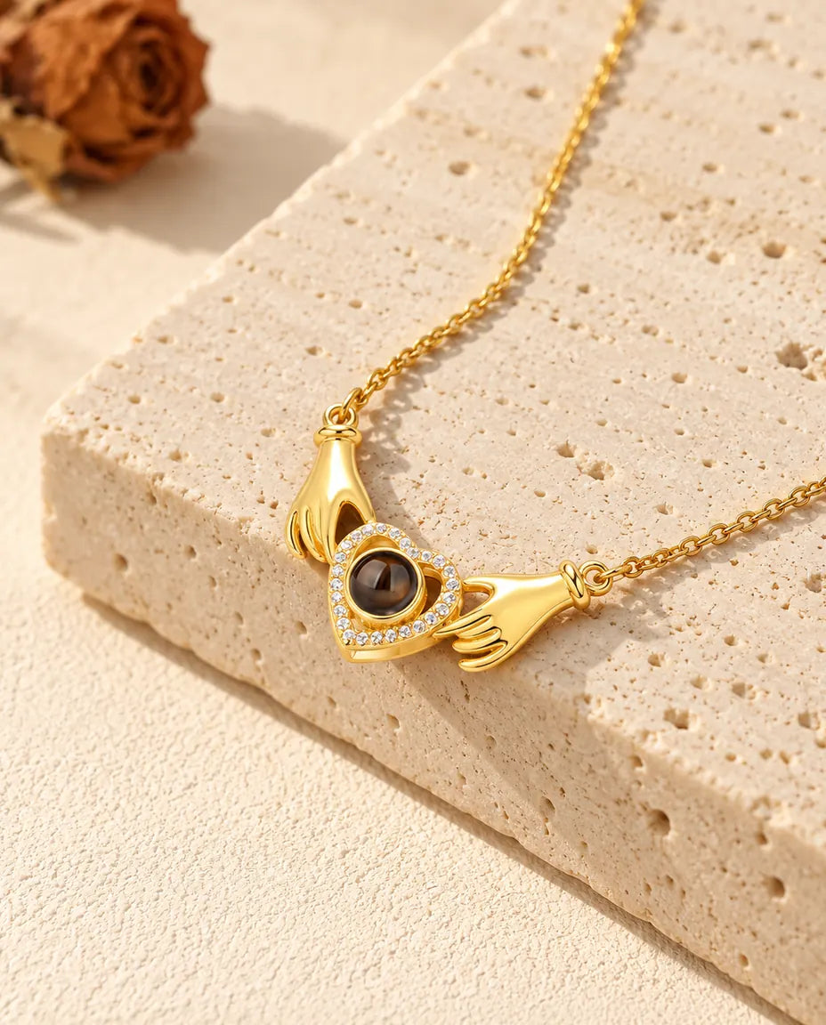 Gold tone photo projection necklace with two hands holding a cubic zirconia heart on travertine