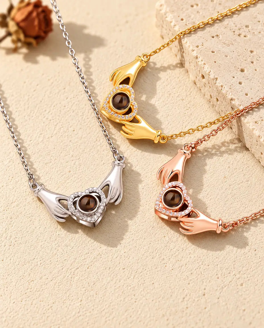 Silver, gold tone and rose gold tone hands holding heart necklaces arranged on plaster and travertine