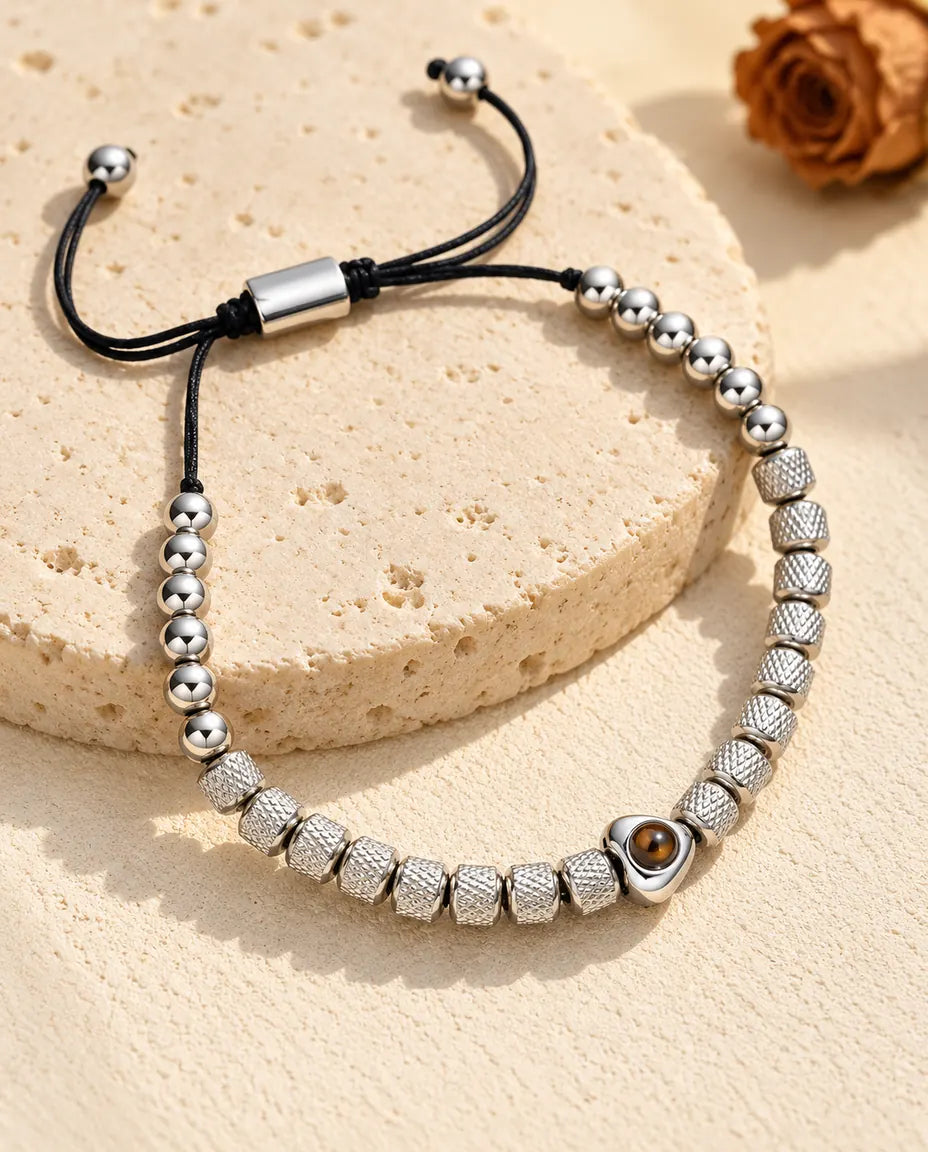 Personalized heart photo projection beaded bracelet in silver tone with textured barrel beads, on a travertine slab