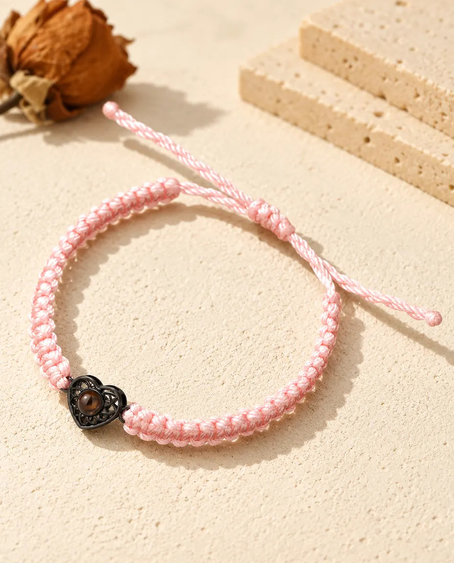 Pink braided cord bracelet with a black heart charm holding a brown projection stone