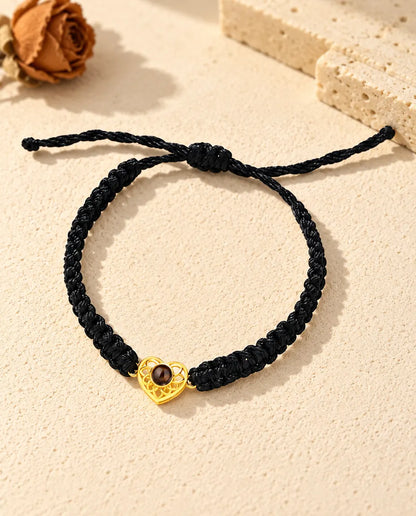 Top view of the gold tone heart charm bracelet on a black braided cord with its sliding knot and cord ends