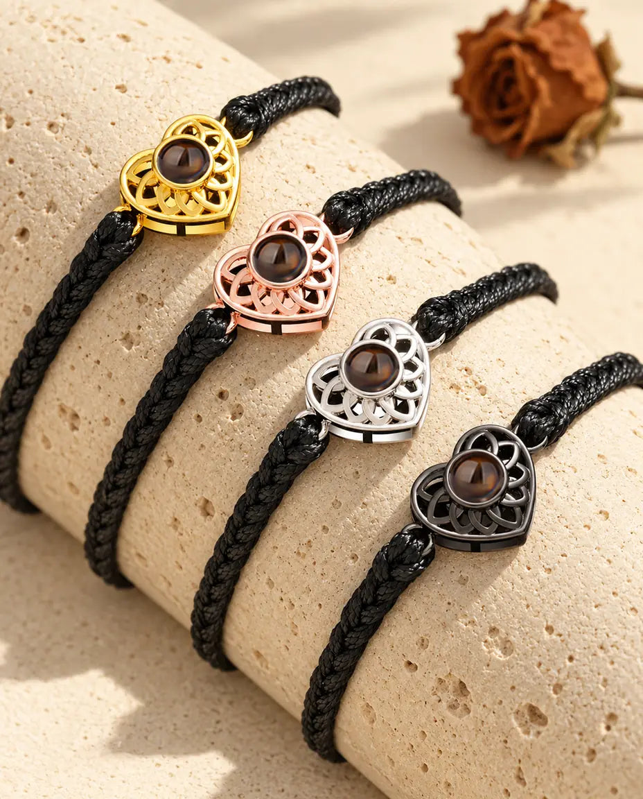 Four black thin braided cord bracelets showing every charm color draped over travertine