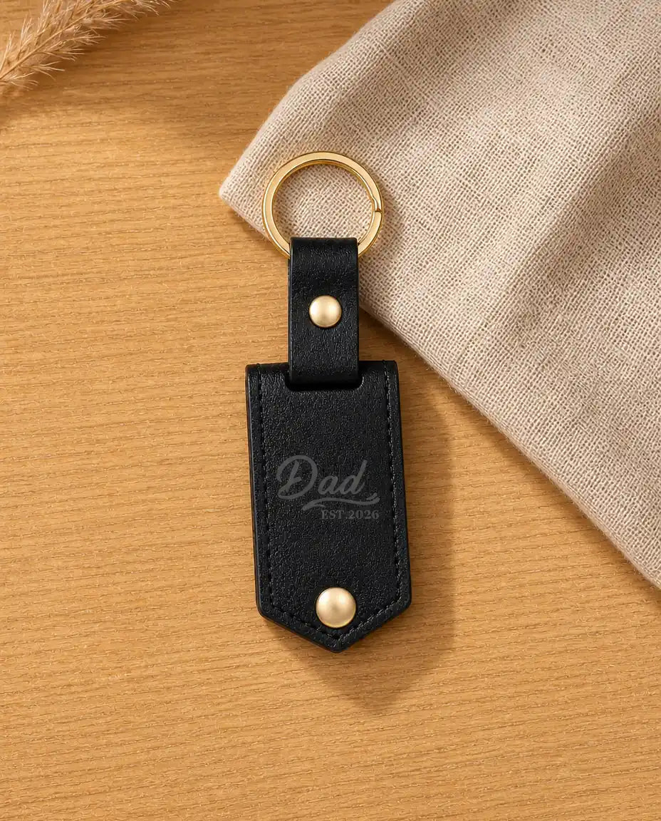 Personalized black faux leather photo keychain engraved with Dad Est. 2026 on a warm wood table