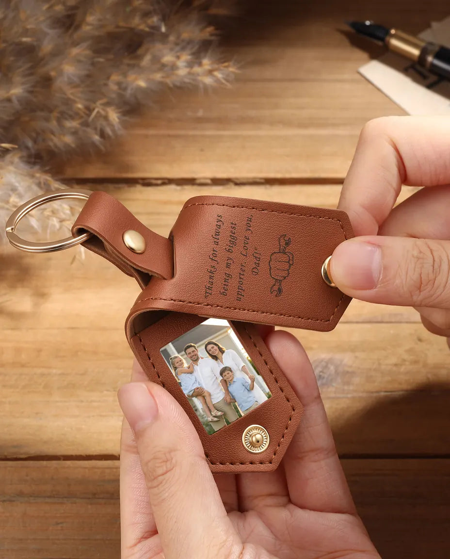 Hands holding an open brown faux leather photo keychain with two family photos