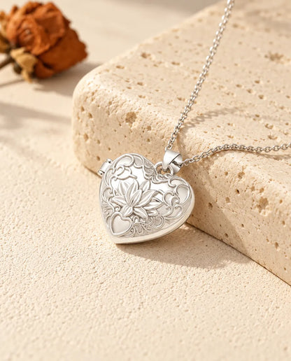 Personalized lotus flower heart photo locket necklace in silver tone with embossed scrollwork, resting on a travertine block